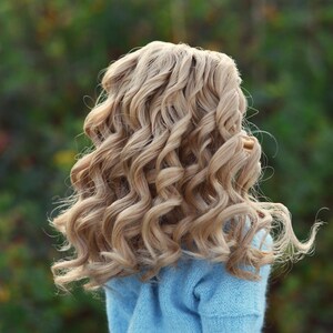 May include: A doll with long, curly, light blonde hair wearing a light blue sweater.