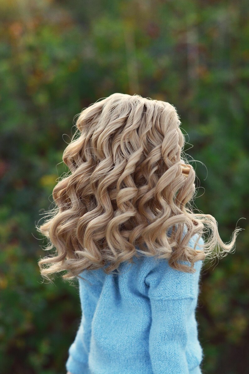 May include: A doll with long, curly, light blonde hair wearing a light blue sweater.