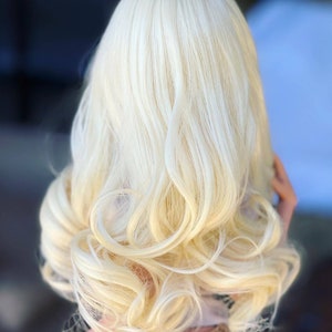May include: A long, wavy, platinum blonde wig with loose curls. The wig is styled in a way that creates volume and movement.