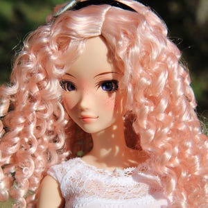 May include: A doll with long, curly, pink hair. The doll is wearing a white lace dress. The doll has blue eyes and freckles.