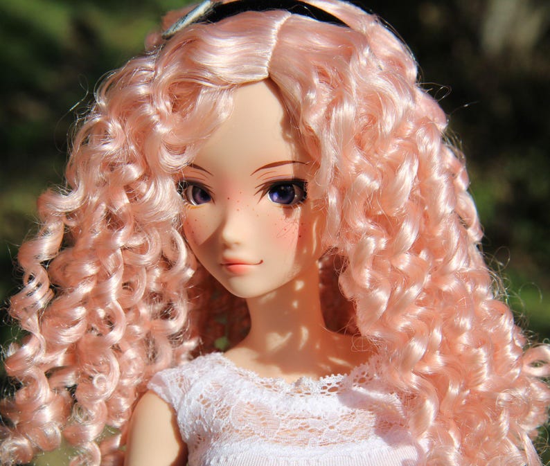 May include: A doll with long, curly, pink hair. The doll is wearing a white lace dress. The doll has blue eyes and freckles.