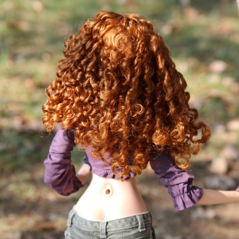 May include: A doll with long, curly, auburn hair wearing a purple shirt and blue jeans.