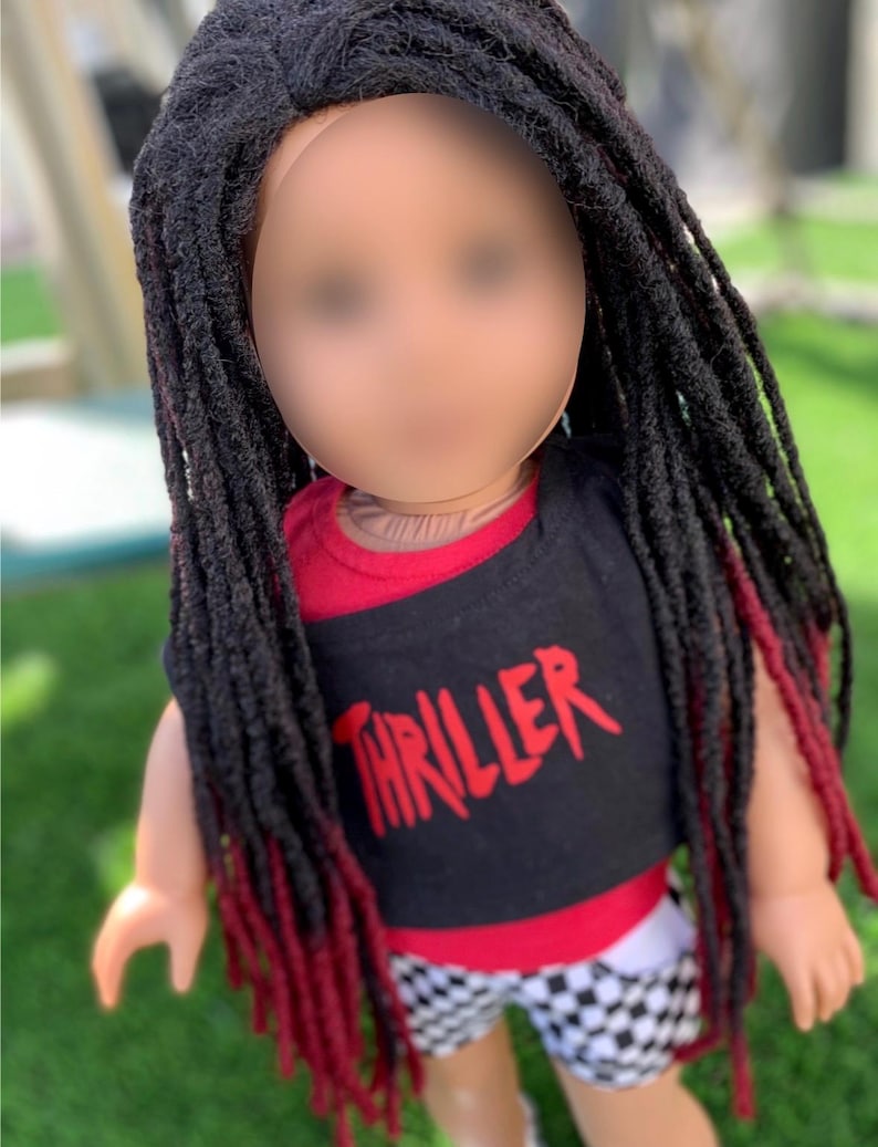 May include: A doll with long black dreadlocks with red tips. The doll is wearing a black t-shirt with the word "THRILLER" in red, a red and black top, and black and white checkered shorts.