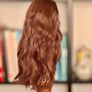 May include: A long, wavy, brown wig with a slight curl at the ends. The wig is styled in a casual, effortless look.