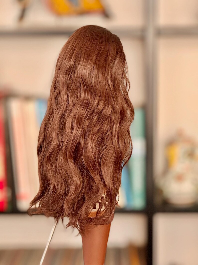May include: A long, wavy, brown wig with a slight curl at the ends. The wig is styled in a casual, effortless look.