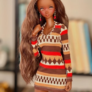 May include: A doll with long brown hair wearing a brown, red, and white patterned dress with long sleeves. The doll has brown skin and is wearing red earrings.