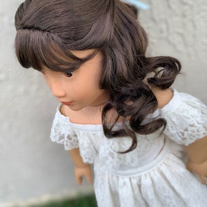 May include: A doll with long brown curly hair wearing a white off-the-shoulder lace dress.