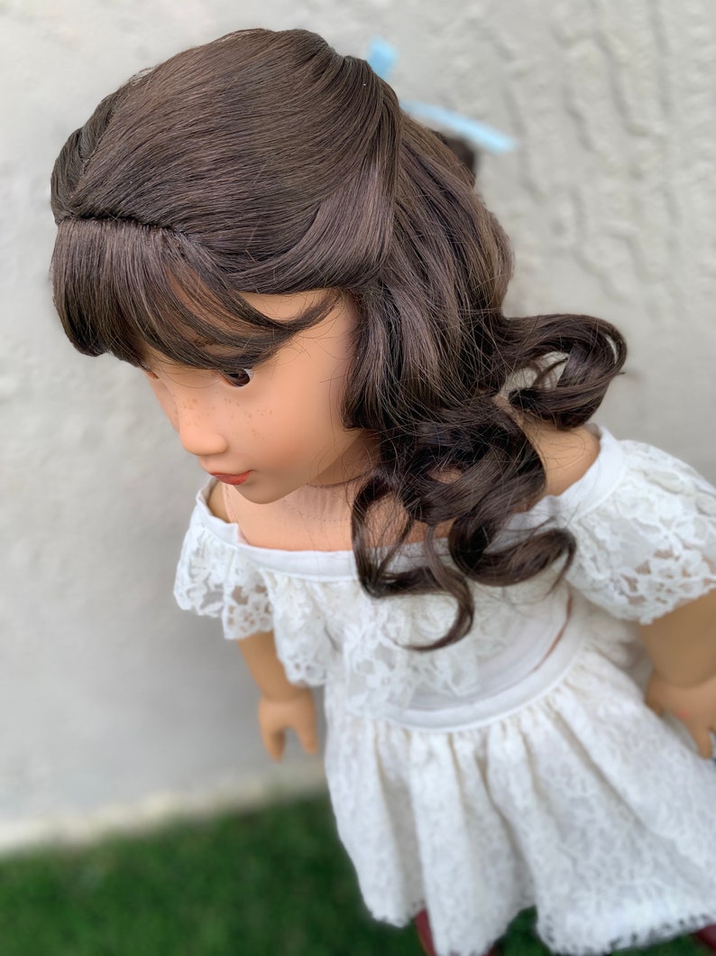 May include: A doll with long brown curly hair wearing a white off-the-shoulder lace dress.