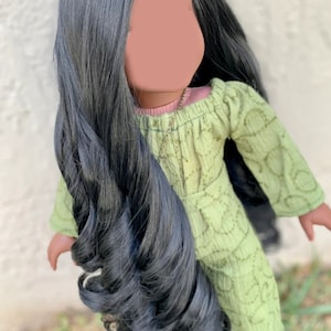 May include: A doll with long, black, curly hair wearing a green dress with a pink undershirt and a gold necklace.