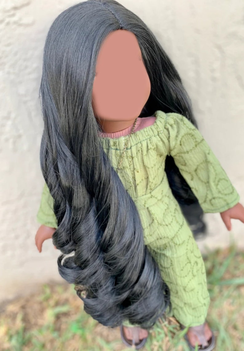 May include: A doll with long, black, curly hair wearing a green dress with a pink undershirt and a gold necklace.