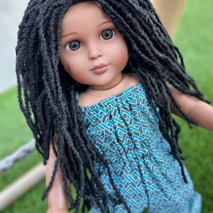 Puede incluir: Una muñeca con largas rastas negras que lleva un mono estampado azul y verde.