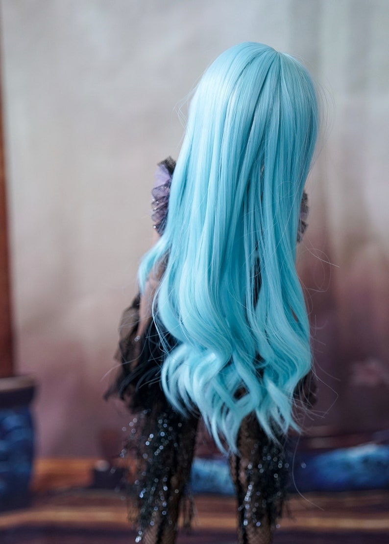 Puede incluir: Una mu&ntilde;eca con el pelo largo, ondulado y azul claro. La mu&ntilde;eca lleva un vestido negro con detalles brillantes.