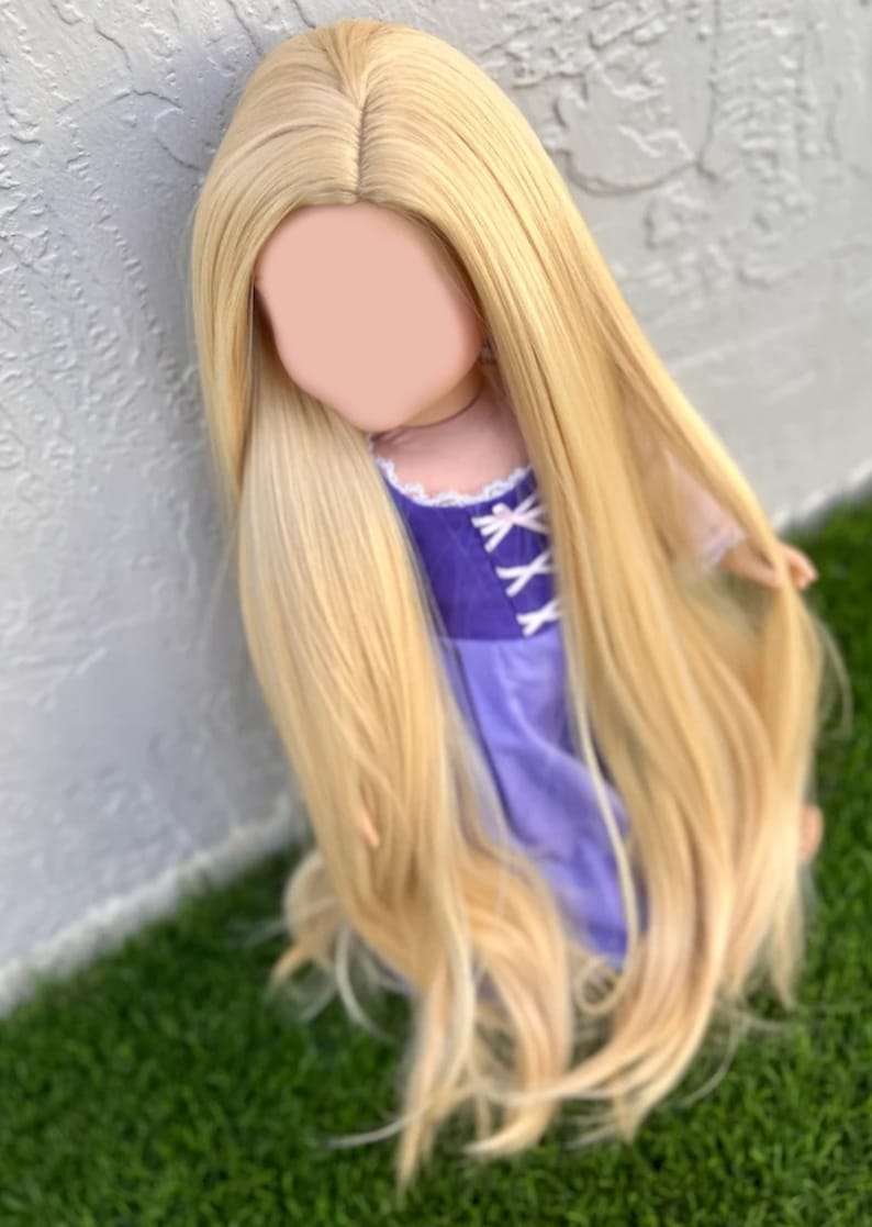 May include: A doll with long, flowing, blonde hair. The doll is wearing a purple dress with white accents. The hair is styled to cascade down the doll's body. The doll is positioned against a white wall and green grass.