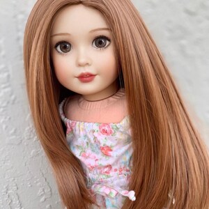 May include: A doll with long, straight, light brown hair wearing a pink and white floral dress.