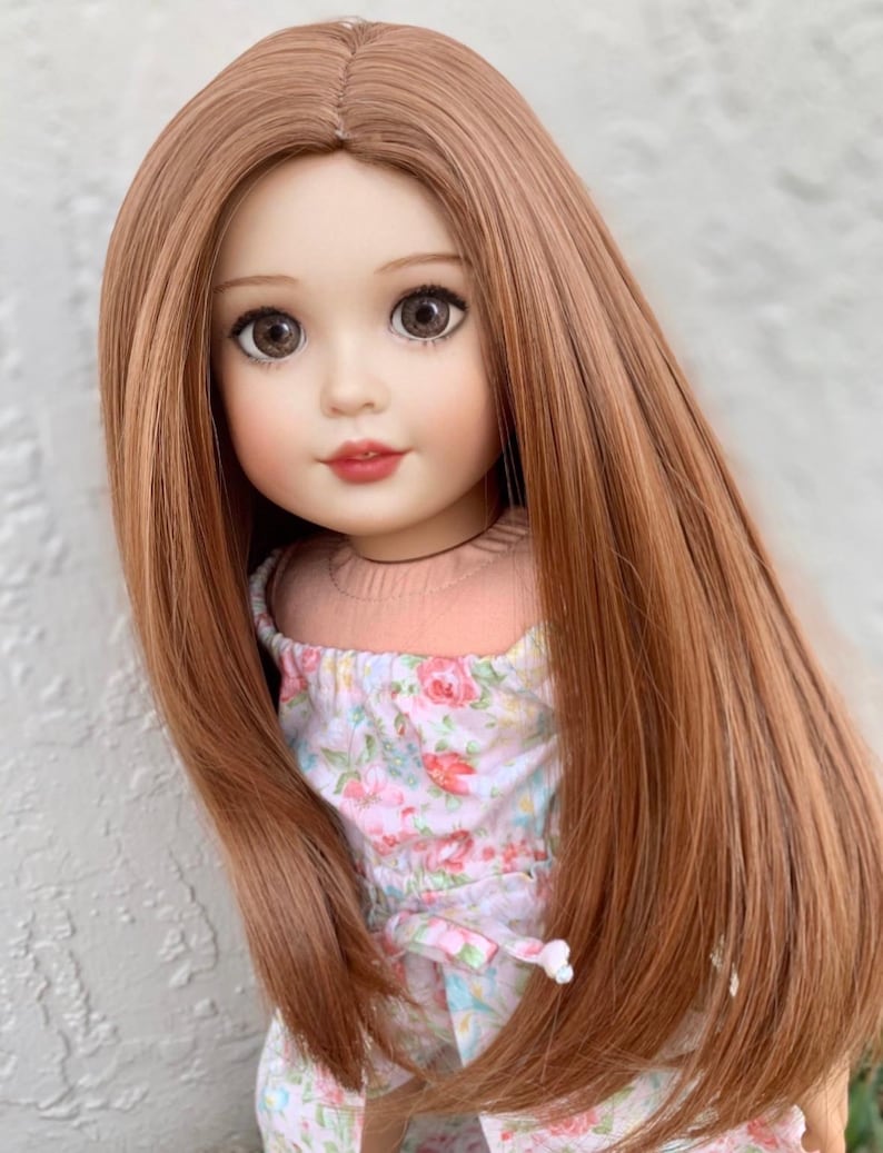 May include: A doll with long, straight, light brown hair wearing a pink and white floral dress.