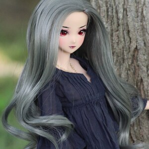 May include: A doll with long, wavy, silver-grey hair wearing a dark blue, ruffled blouse. The doll has red eyes and a delicate face.