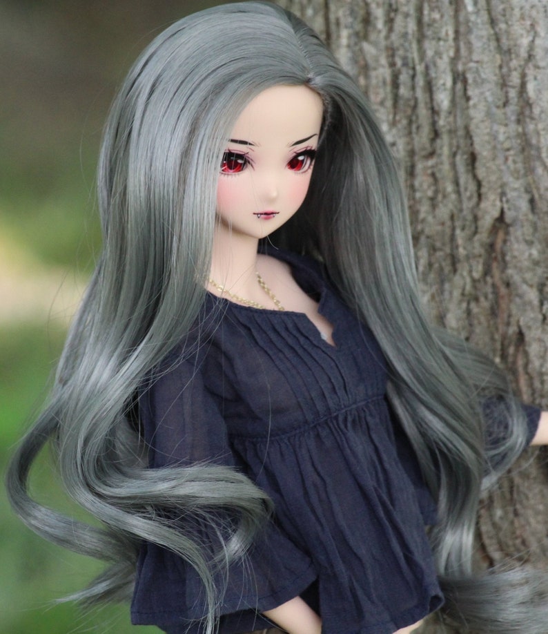 May include: A doll with long, wavy, silver-grey hair wearing a dark blue, ruffled blouse. The doll has red eyes and a delicate face.