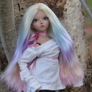 May include: A doll with long, white, pink, blue, and purple hair wearing a white off-the-shoulder sweater with a pink ribbon tied around the waist.