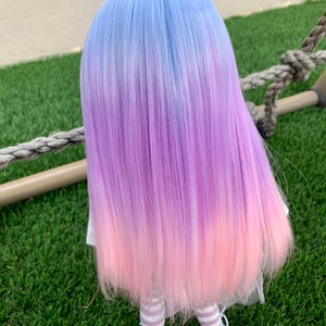 May include: A doll with long, straight, ombre hair that transitions from light blue to purple to pink. The doll is wearing a white dress with a pink tulle skirt and white and purple striped tights.