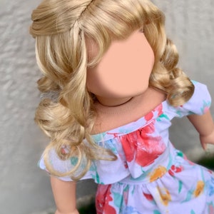 May include: A doll with blonde, wavy hair styled in an updo. The doll is wearing a white dress with a floral pattern in red, blue, and yellow. The dress has an off-the-shoulder neckline.