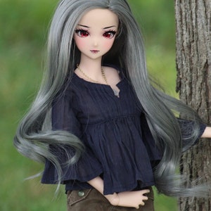 May include: A doll with long, flowing silver hair, wearing a dark blue blouse and brown pants. The doll has red eyes and a delicate face.