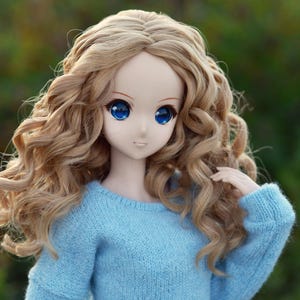 May include: A doll with long, curly, light brown hair wearing a light blue sweater.