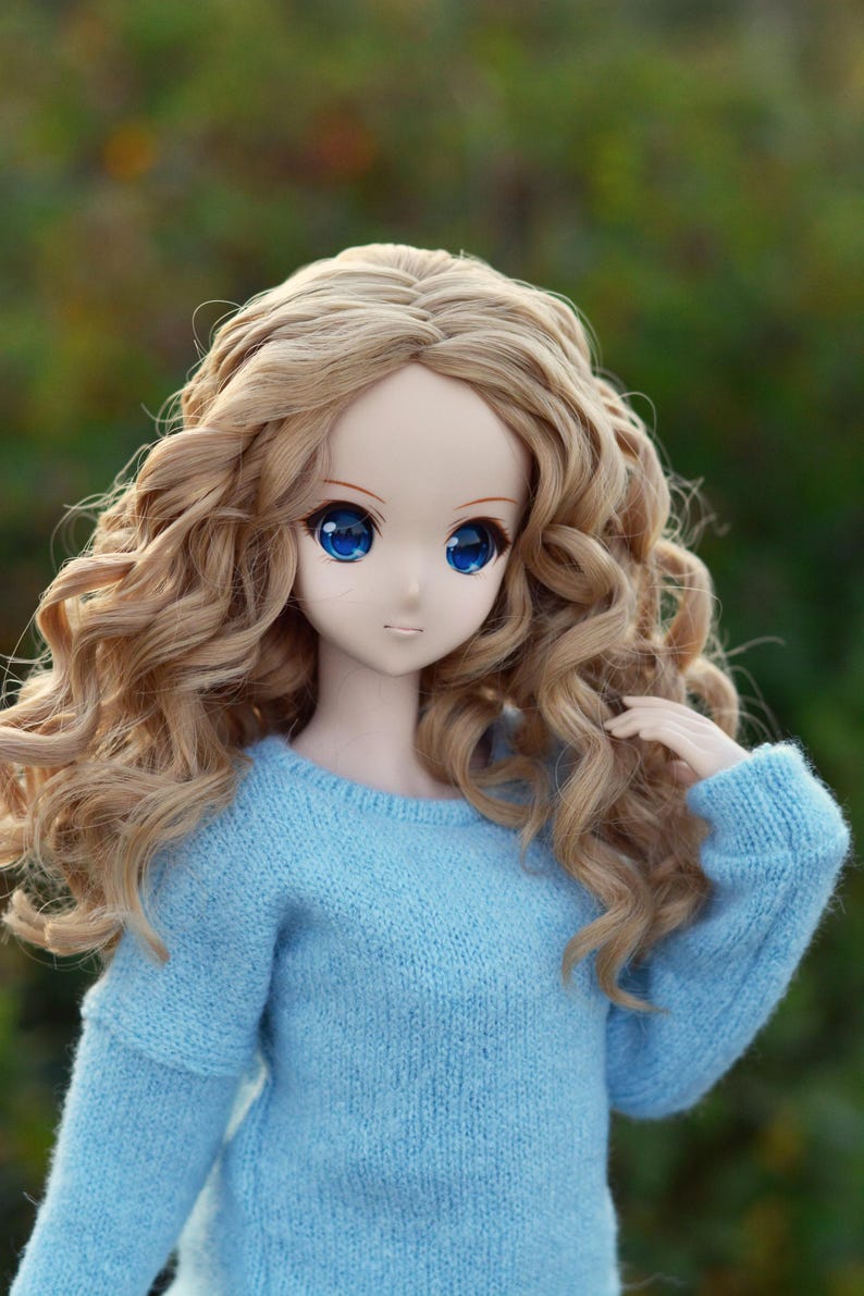 May include: A doll with long, curly, light brown hair wearing a light blue sweater.