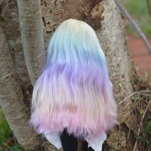 May include: A doll with long, wavy hair in shades of blue, purple, and pink. The hair is styled in a loose, flowing manner.