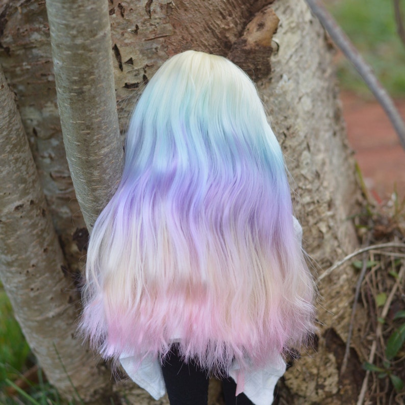 May include: A doll with long, wavy hair in shades of blue, purple, and pink. The hair is styled in a loose, flowing manner.