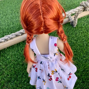 May include: A doll with long, red hair in braids wearing a white dress with a cherry print.