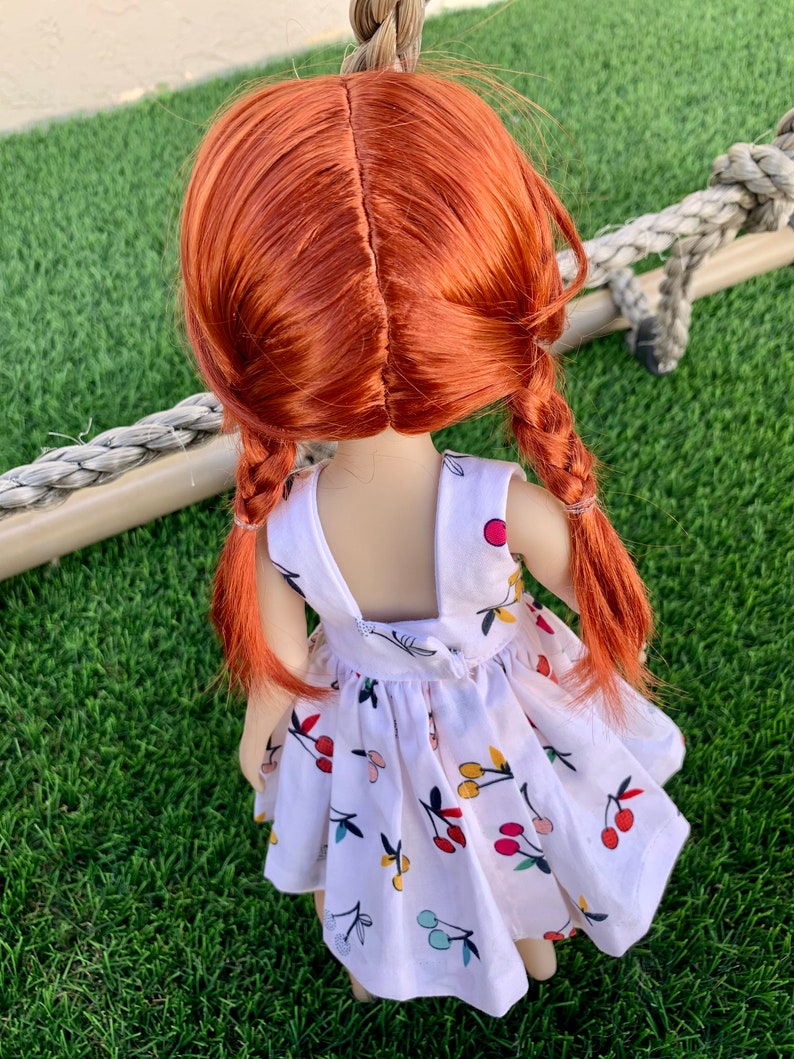 May include: A doll with long, red hair in braids wearing a white dress with a cherry print.