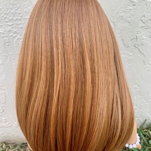May include: A doll with long, straight, light brown hair. The hair is styled in a bob with layers. The doll is wearing a floral print dress.