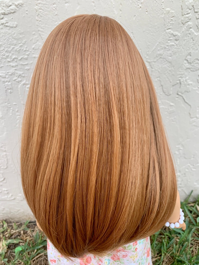 May include: A doll with long, straight, light brown hair. The hair is styled in a bob with layers. The doll is wearing a floral print dress.