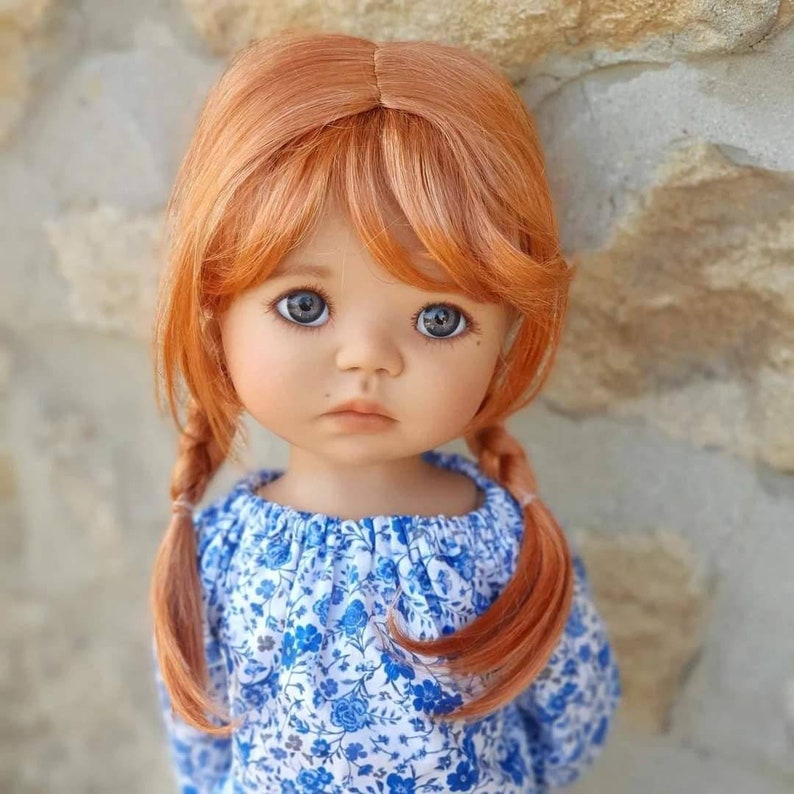 May include: A doll with long, straight, auburn hair styled in two braids. The doll is wearing a blue and white floral dress with an off-the-shoulder neckline.