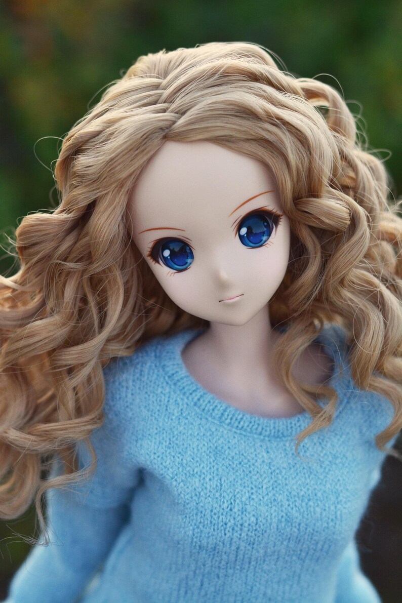 May include: A doll with long, curly blonde hair wearing a light blue sweater.