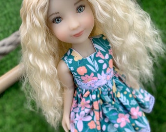 May include: A doll with long, blonde, curly hair wearing a green dress with a floral pattern. The dress has a white lace trim.