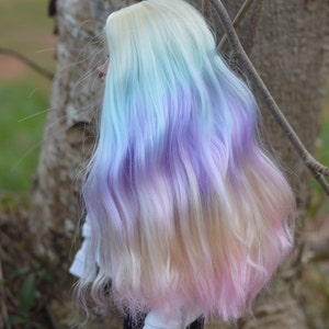 May include: A doll with long, wavy hair that is ombre dyed in shades of light blue, purple, and pink.