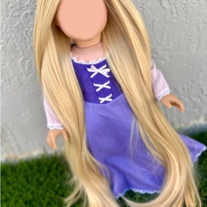 May include: A doll with long, flowing blonde hair and a purple dress. The dress has a bodice with white criss-cross ribbon detail. The doll's sleeves are light pink with white lace trim. The doll is posed on green grass.