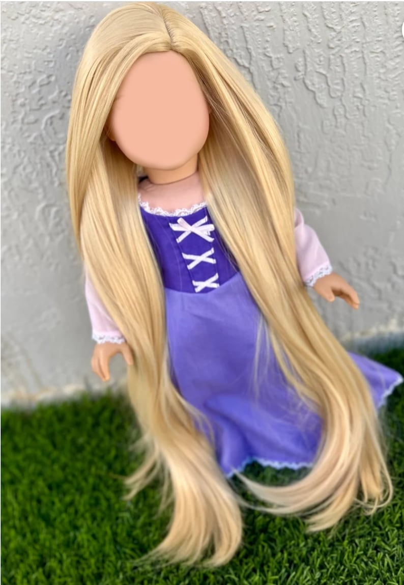 May include: A doll with long, flowing blonde hair and a purple dress. The dress has a bodice with white criss-cross ribbon detail. The doll's sleeves are light pink with white lace trim. The doll is posed on green grass.