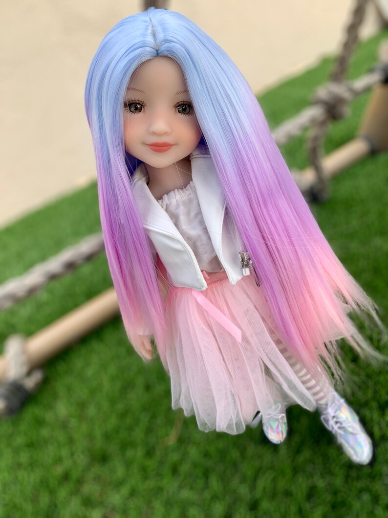 May include: A doll with long, ombre hair that transitions from light blue to pink. The doll is wearing a white jacket, a pink tulle skirt, and white and black striped tights.