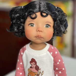Peut inclure: Une poupée aux cheveux bouclés foncés portant une chemise rose et blanche avec un motif de Belle de La Belle et la Bête.