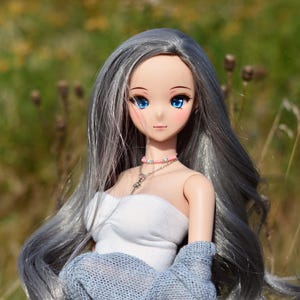 May include: A doll with long, silver hair, blue eyes, and a light pink blush. She is wearing a white tank top, a light blue knitted cardigan, and a floral skirt.