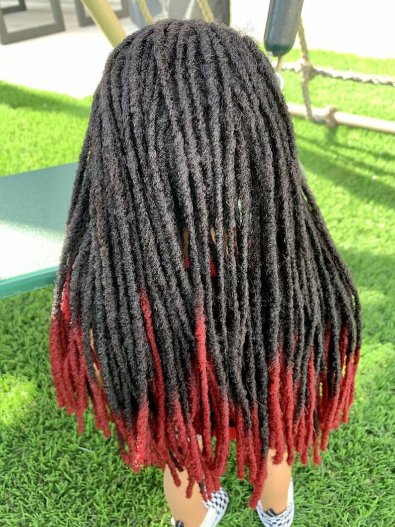 May include: A head of black dreadlocks with red tips. The dreadlocks are long and hang down the back. The hair is styled with a natural look, and the red tips add a pop of colour. The person is wearing checkered shoes.