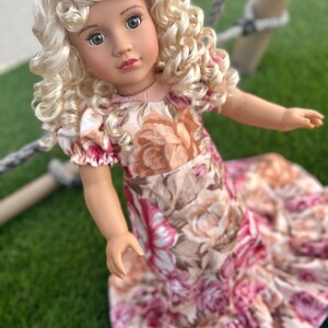 May include: A doll with blonde curly hair wearing a pink and brown floral dress.