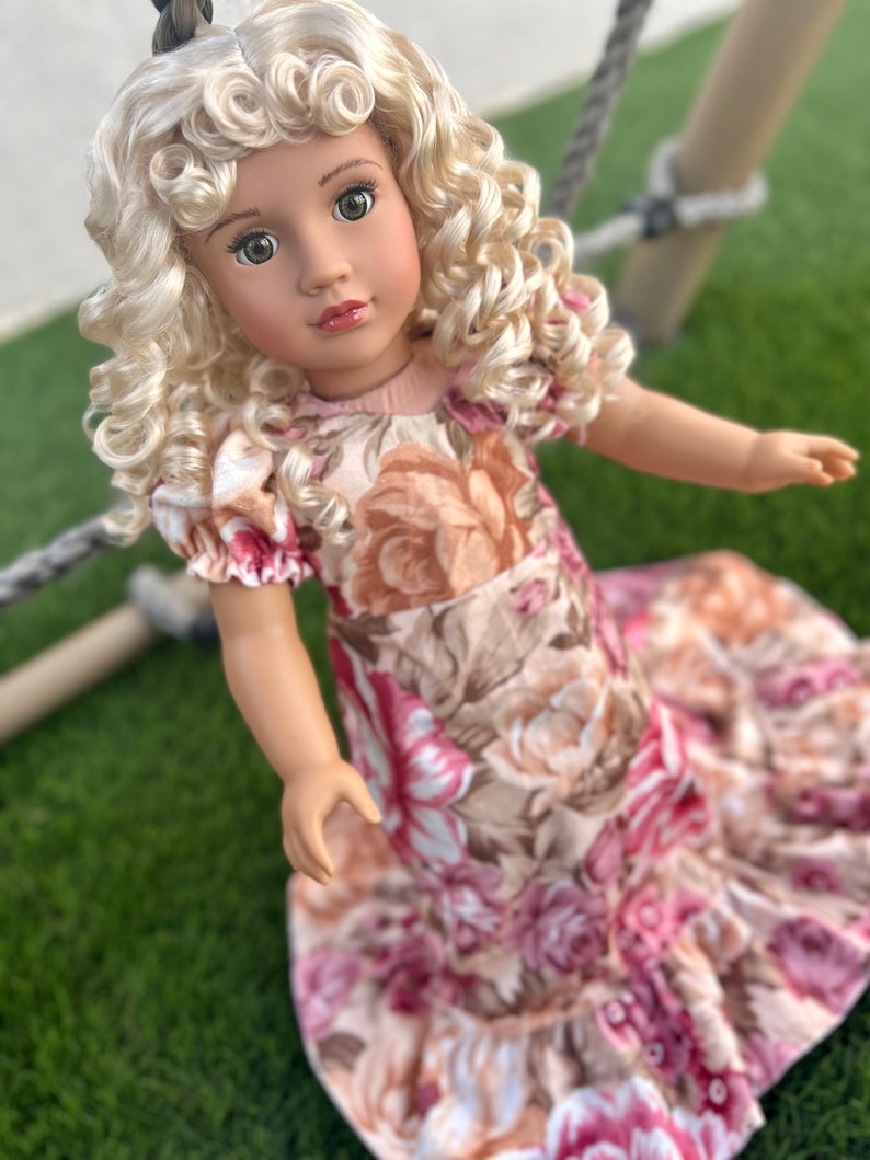 May include: A doll with blonde curly hair wearing a pink and brown floral dress.