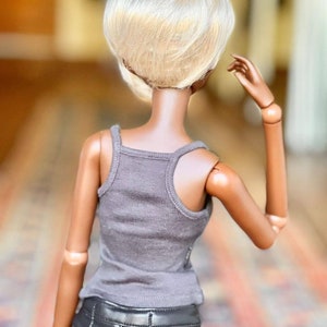 May include: A doll with a short, platinum blonde wig, wearing a gray tank top and black leather pants.