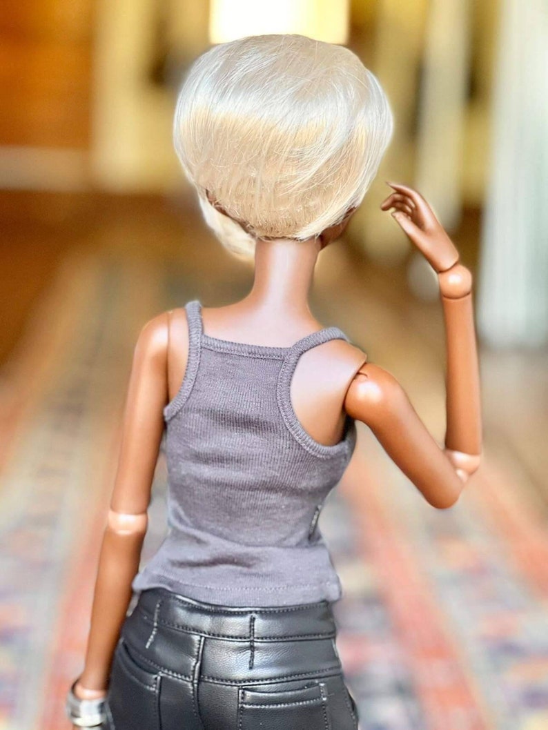 May include: A doll with a short, platinum blonde wig, wearing a gray tank top and black leather pants.