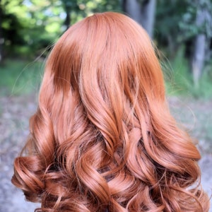 May include: A long, curly, auburn-colored wig. The wig is styled in loose curls and falls to the shoulders.