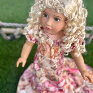 May include: A doll with blonde curly hair wearing a pink and brown floral dress.