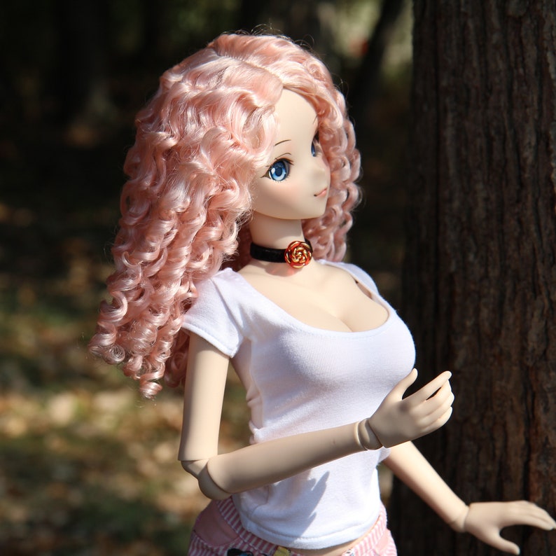 May include: A pink haired doll with blue eyes wearing a white t-shirt and a black choker with a rose charm. The doll is standing next to a tree trunk.